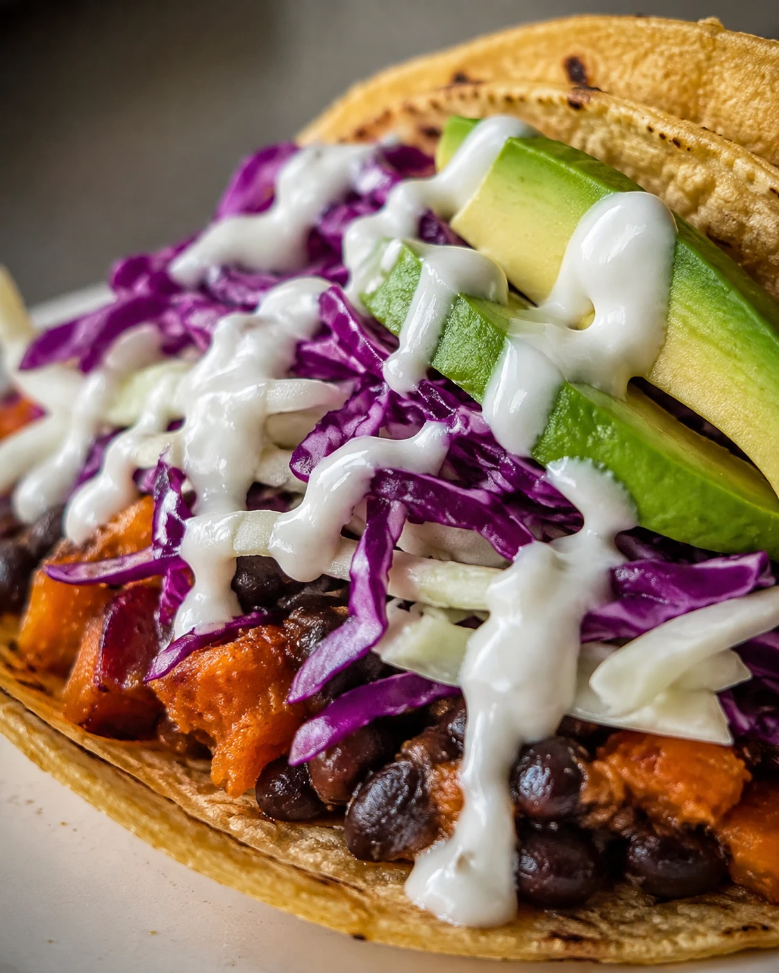 Creamy black bean and sweet potato filling is topped with crisp cabbage, avocado slices, and lime-yogurt sauce in a taco.