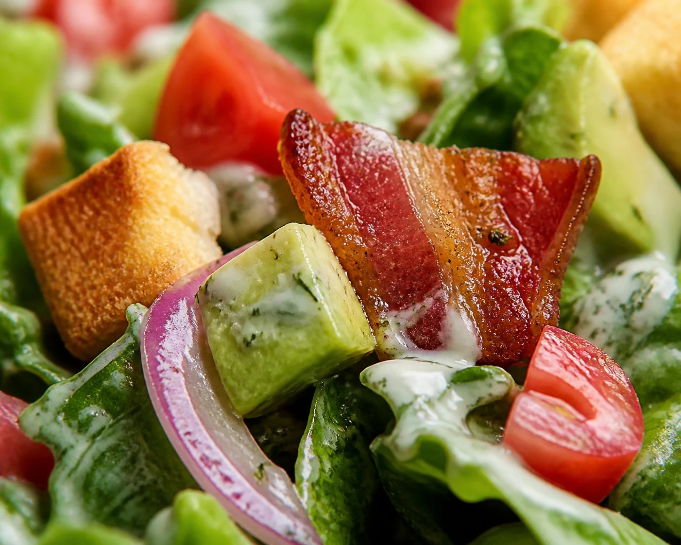 A close chopped salad bite shows romaine, tomato, crisp bacon, avocado, onion, crouton, and herb dressing.