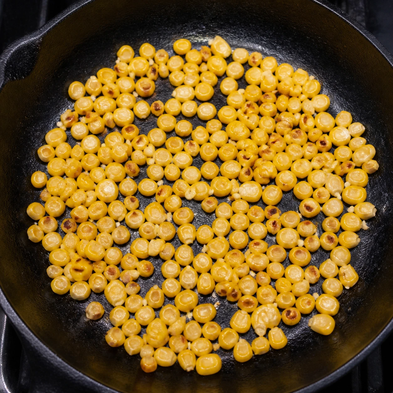 Corn kernels in a single layer begin browning in a hot black cast-iron skillet.
