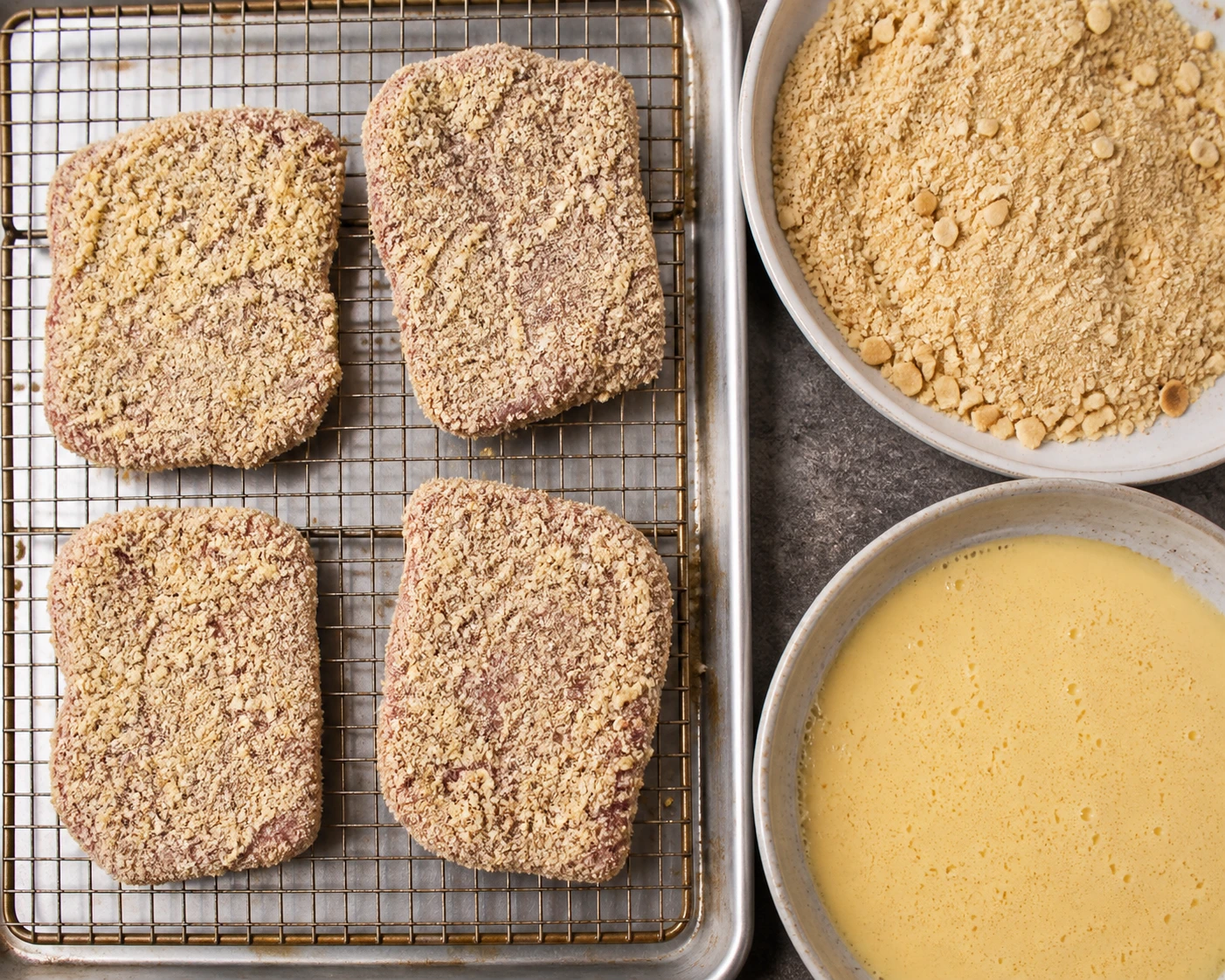 Double-coated cube steaks rest on a wire rack beside the breading station before shallow frying.