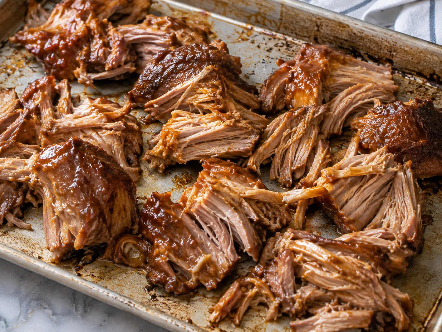 Large pieces of tender pork coated with reduced citrus cooking juices rest loosely on a sheet pan.