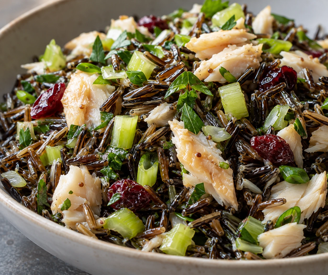 Distinct wild rice grains and large smoked whitefish flakes sit among celery, parsley, scallion, and cranberries.