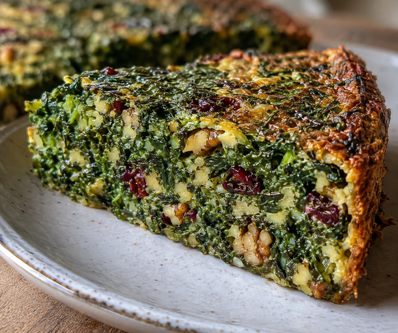 A kuku sabzi wedge shows its green herb interior, toasted walnuts, tart barberries, and browned crisp edge.