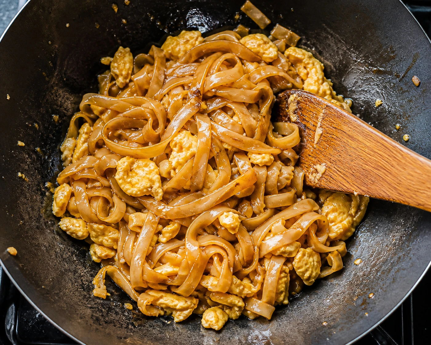 Rice noodles toss with sauce and soft egg curds in a wok during the Pad Thai stir-fry.