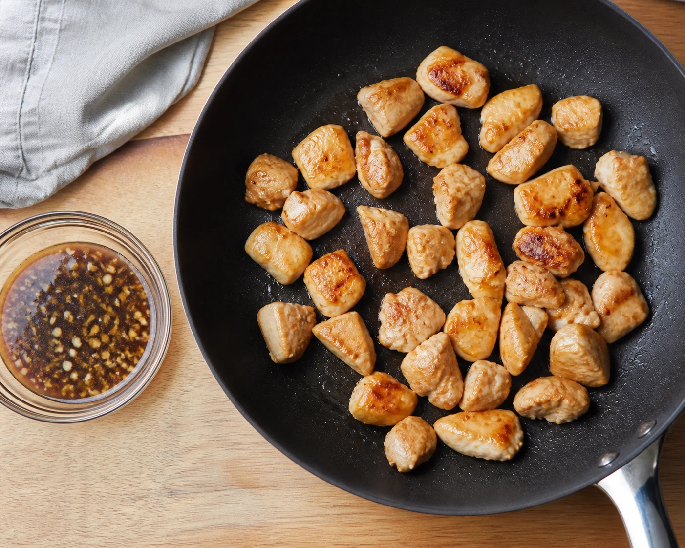 Small chicken pieces brown in a nonstick skillet beside a bowl of homemade teriyaki-style glaze.