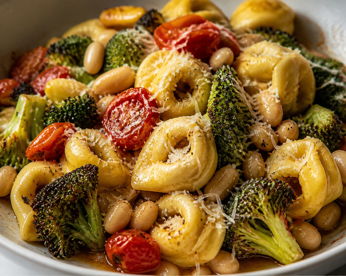 Glossy tortellini is coated with Parmesan beside creamy white beans, burst tomatoes, and browned broccoli.