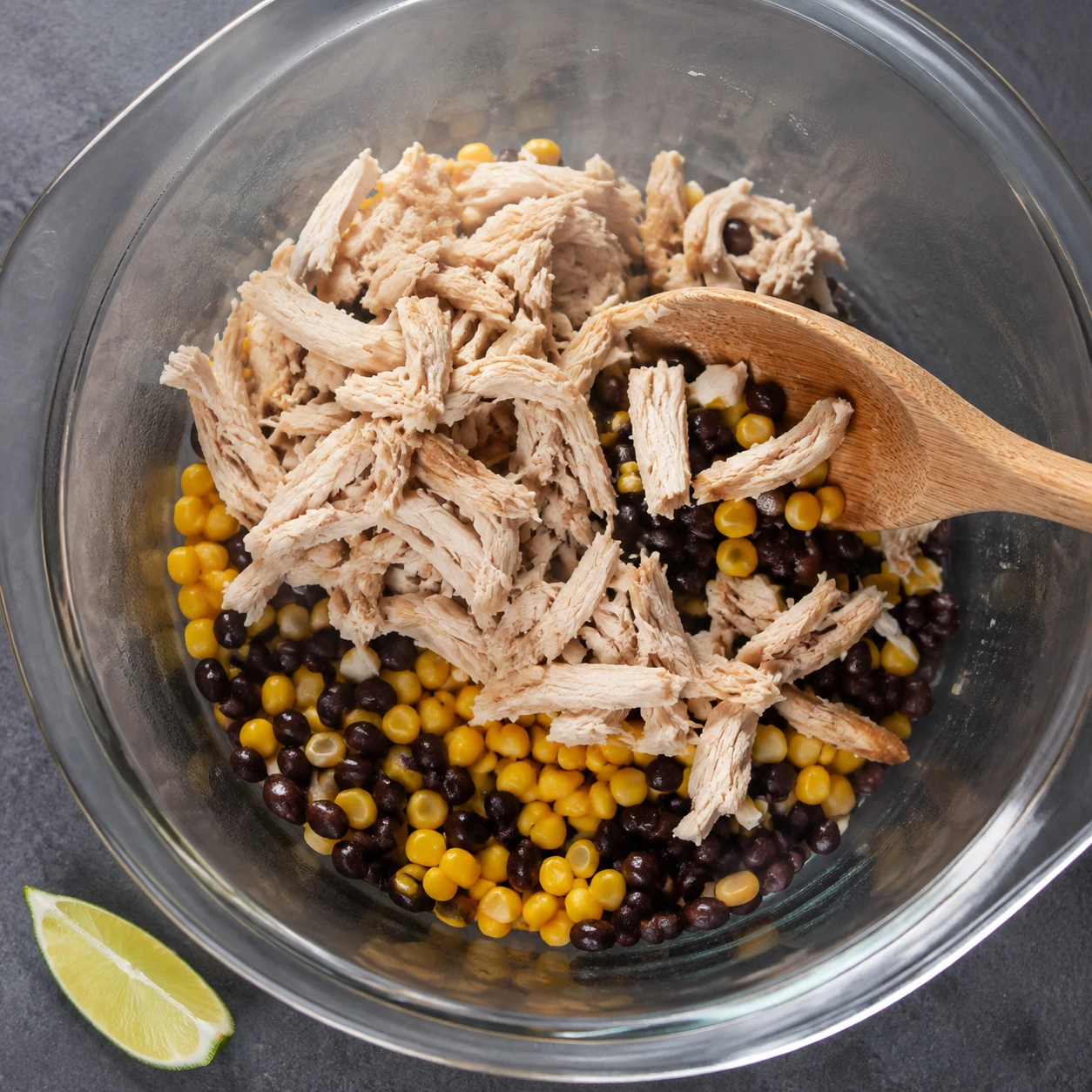 Steaming black beans and corn are folded with shredded rotisserie chicken in a bowl.