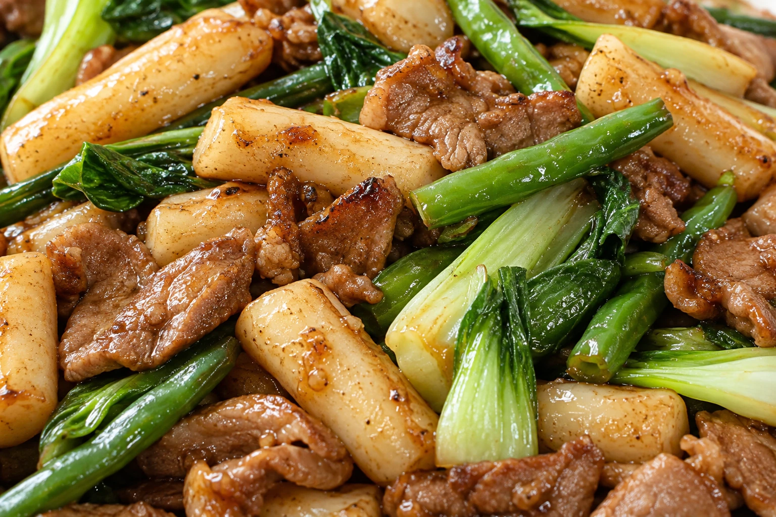 Chewy rice cakes and seared pork sit among crisp green vegetables in a glossy savory coating.